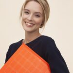 smiling woman standing while holding orange folder