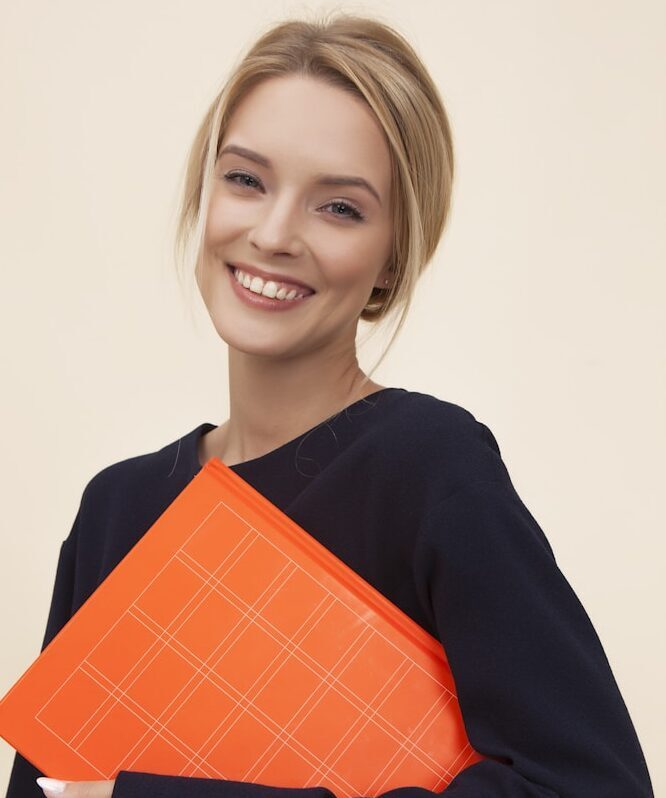 smiling woman standing while holding orange folder